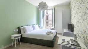 A modern hotel room with a large bed, a small desk, a television, and a balcony with a view of the city. - Italianway - The B Village Business - 35 (Milan)