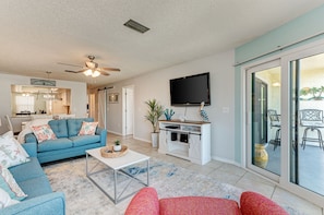 Relax in this open-plan living space with a large flat-screen TV, ceiling fan, and sliding glass door to the outdoor patio.