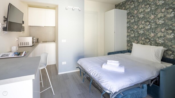 A compact hotel room with a bed, a desk with a chair, a microwave, and a small kitchenette. - Italianway - The B Village Superior - 40 (Milan)