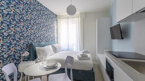 Ein modernes Hotelzimmer mit einem Bett, einem Essbereich mit Tisch und Stühlen, einem an der Wand befestigten Fernseher und einem Fenster mit Vorhängen.