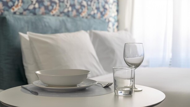 Ein Esstisch mit Schüssel, Glas und Tischset, einer Gabel sowie einem Kissen im Hintergrund.