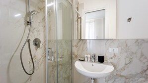 A modern bathroom with a glass-enclosed shower, a white sink, and a marble-tiled wall. - Italianway - The B Village Business - 30 (Milan)