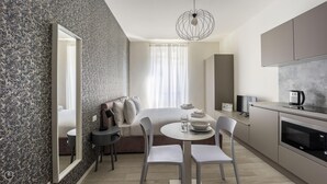A compact hotel room with a bed, a dining table with chairs, a kitchen area with a coffee maker, and a large mirror. - Italianway - The B Village Business - 34 (Milan)