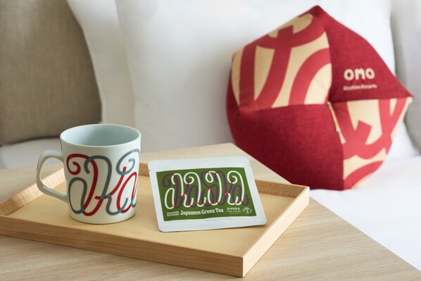 Una taza blanca con letras rojas y verdes, un cojín rojo y beige, y una tarjeta con texto japonés sobre una bandeja de madera.