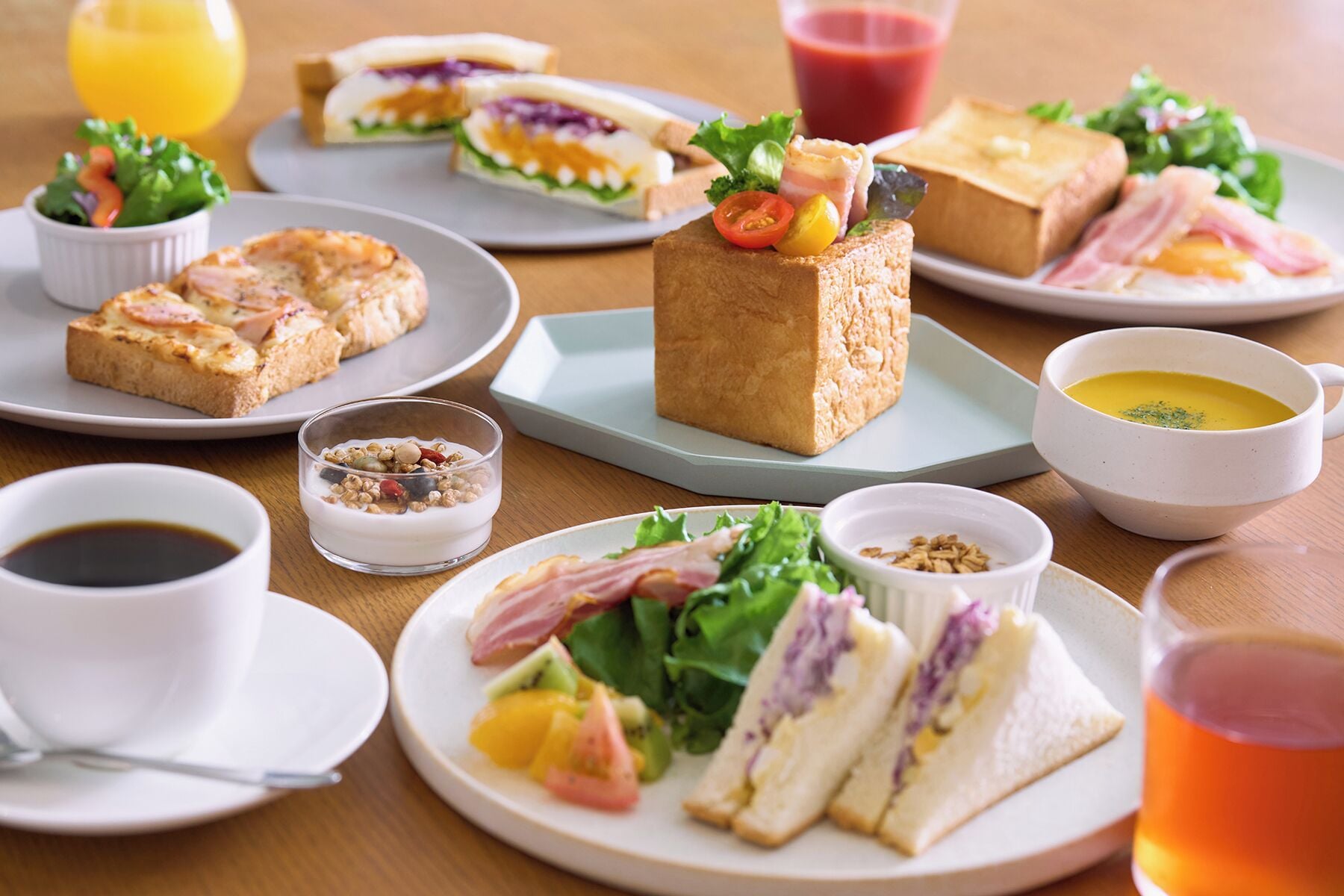 A variety of food items including sandwiches, a block of cheese, and a bowl of soup on a table.