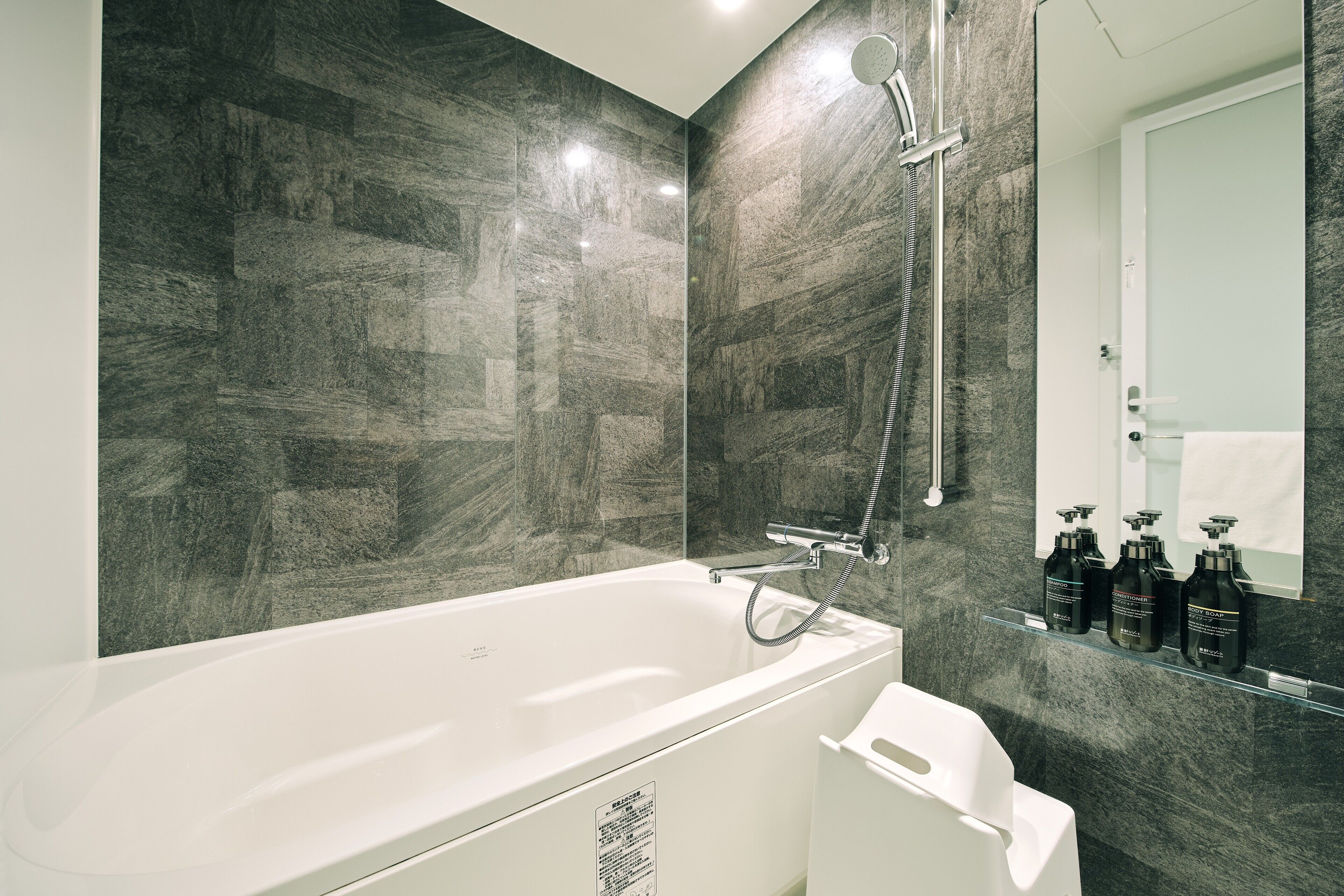A modern bathroom with a large bathtub, a shower, and a mirror with a shelf holding toiletries.
