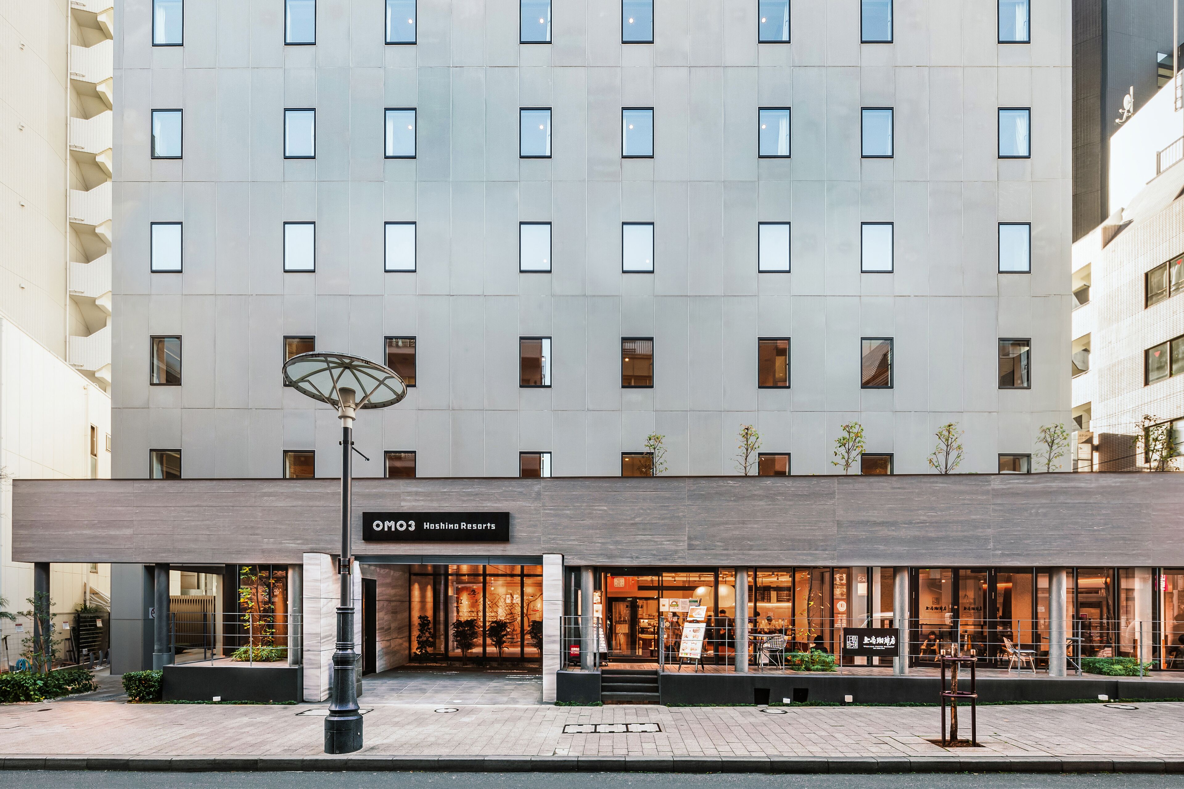 A modern hotel with a large glass facade, a sign for "Hashing Resorts," and a well-maintained outdoor area with seating.