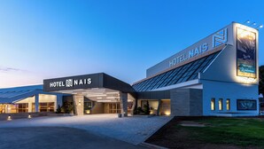 A modern hotel with a prominent sign, large glass windows, and a well-lit entrance. - HOTEL NAIS (Vrtiste)