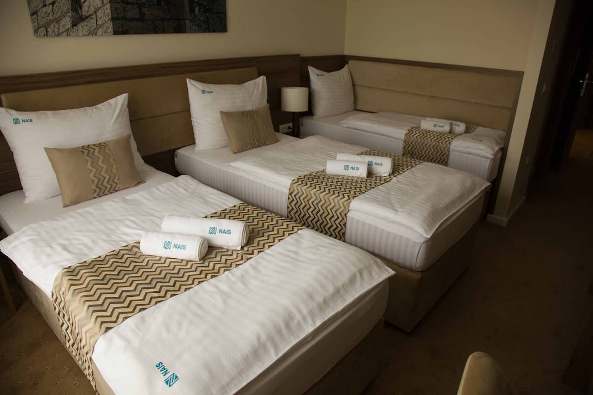 A hotel room with three beds, each with a Nais pillows and a Nais blanket.