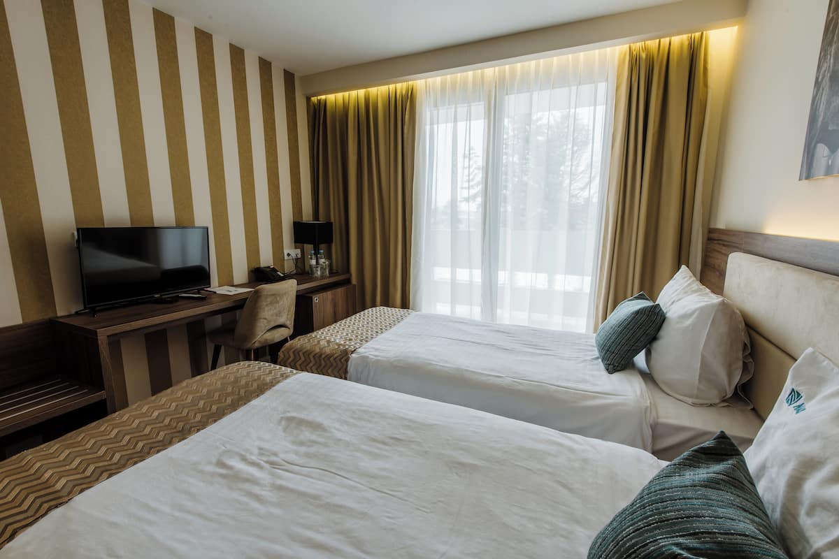 A hotel room with two beds, a desk with a TV, and a window with curtains.