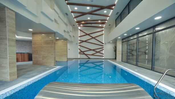 An indoor swimming pool with a modern design, featuring a clear blue pool, a wooden ceiling structure, and glass walls on one side. - HOTEL NAIS (Vrtiste)