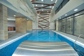 Una piscina interior de diseño moderno, con aguas azules cristalinas, una estructura de techo de madera y paredes de vidrio en un lateral.