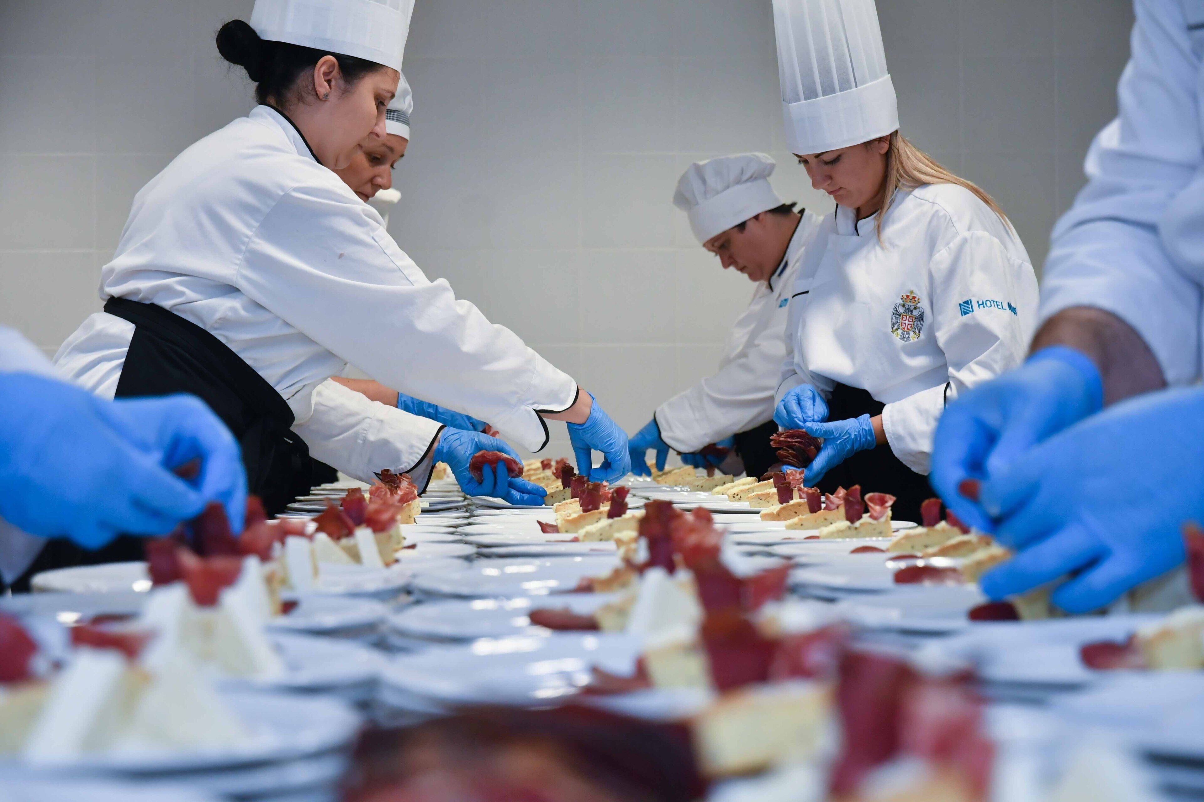 A group of chefs in white uniforms and hats preparing food in a kitchen.