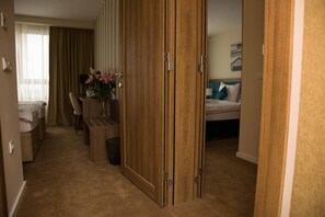 Habitación de hotel con un armario de madera, una cama, un escritorio con una silla y una pequeña mesa con un florero.