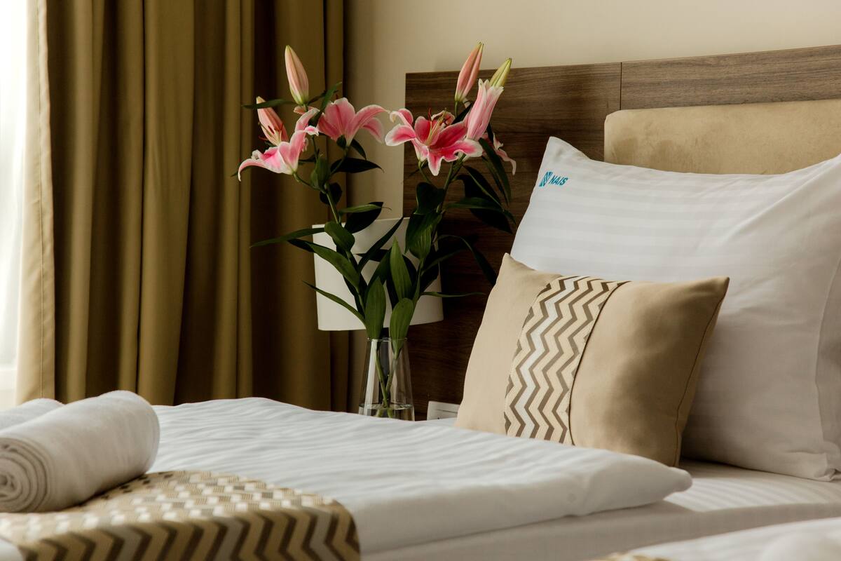 A neatly made bed with a patterned bedspread, a vase with pink flowers, and a pillow with a chevron design.