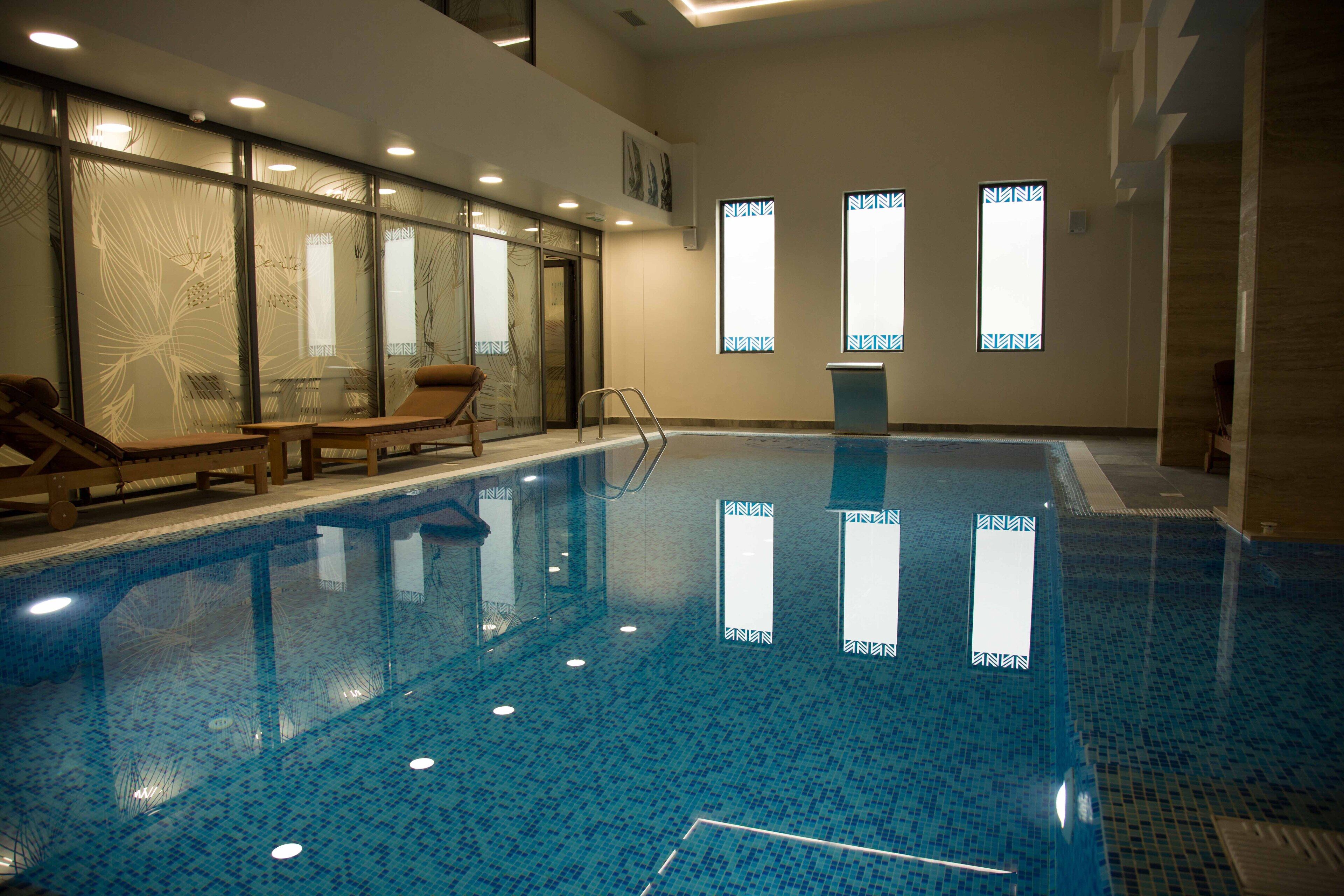 Une piscine intérieure avec des parois en verre transparent, quelques chaises longues et un petit escalier pour y accéder.