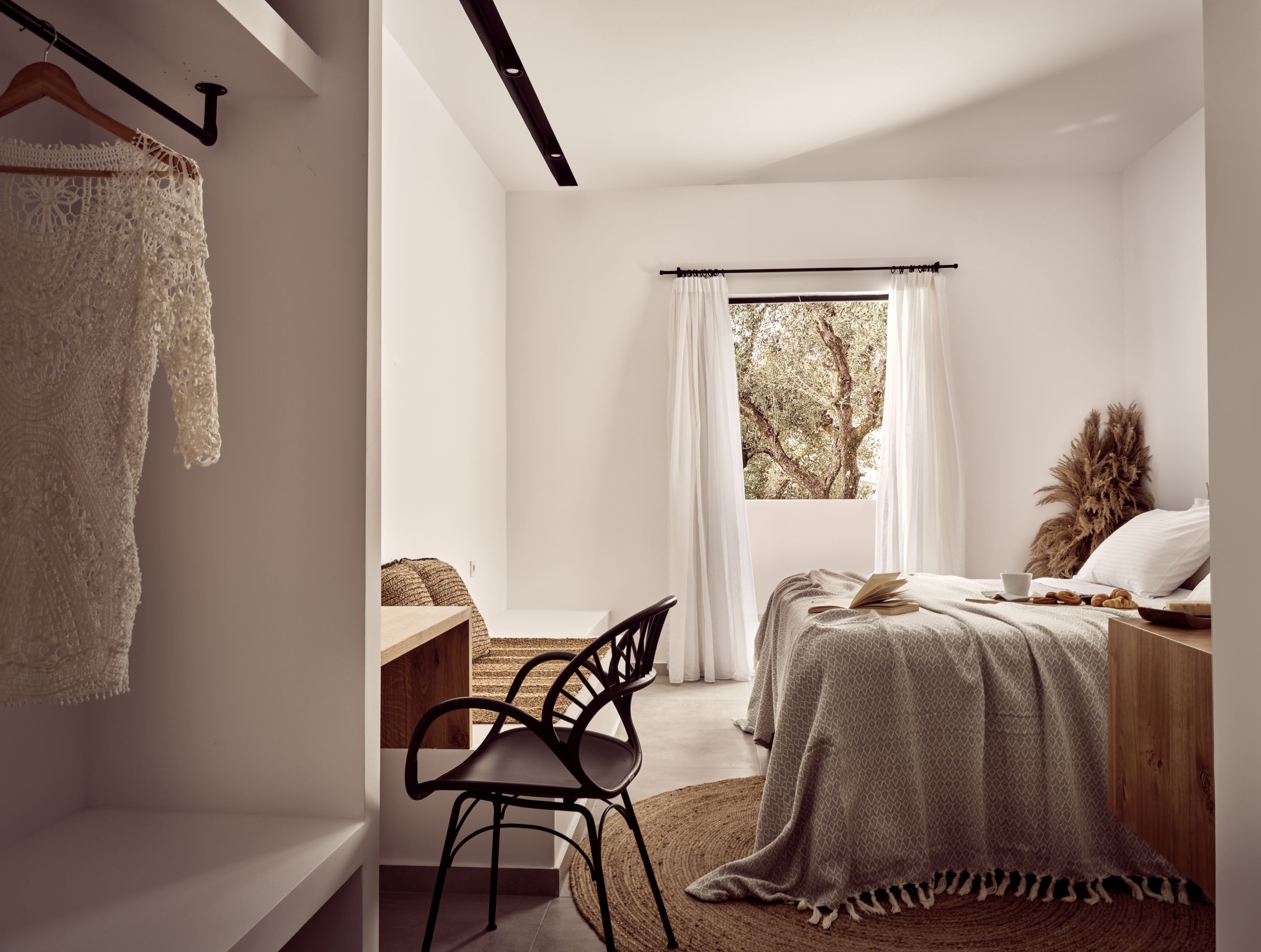 A minimalist bedroom with a bed, a chair, a desk, and a window with curtains.