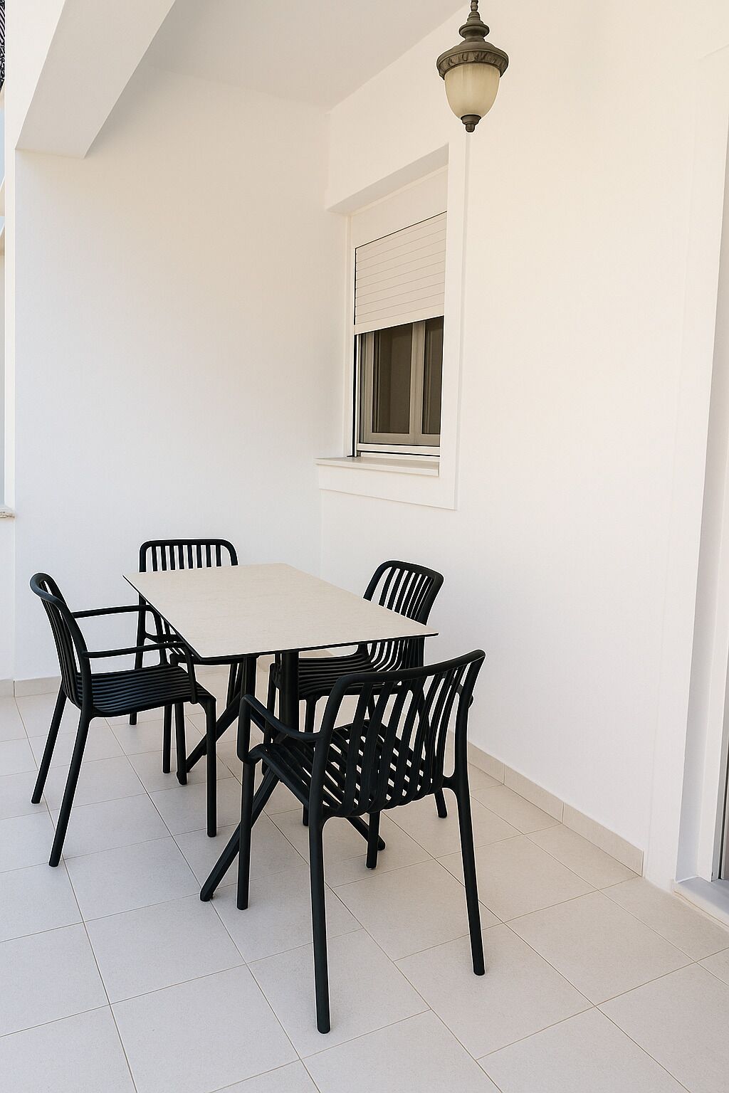 A dining area with a white table and black chairs, a window with blinds, and a hanging light fixture.