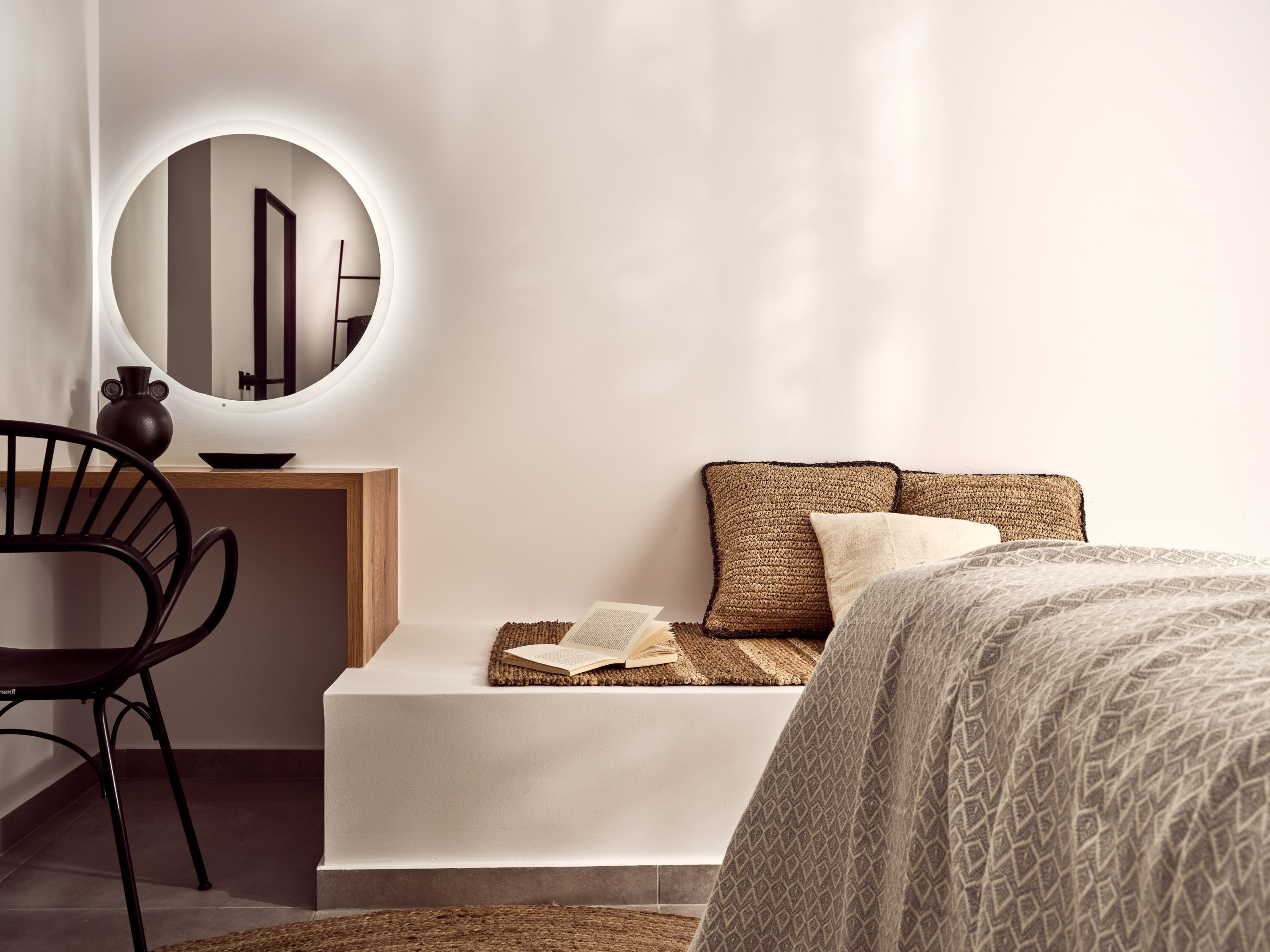 Une chambre moderne avec un lit, une table de chevet, une chaise et un miroir rond.