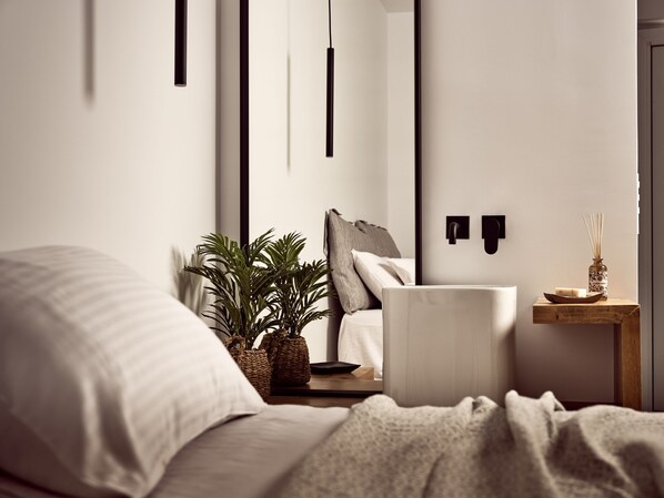A modern bedroom with a bed, bedside plants, a nightstand, a mirror, and a wall-mounted light fixture. - Sanpiero Island (Zakynthos)