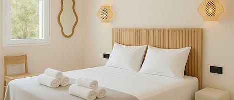Un letto rifatto con lenzuola bianche e asciugamani arrotolati, una testiera in legno e due lampade fissate alla parete.