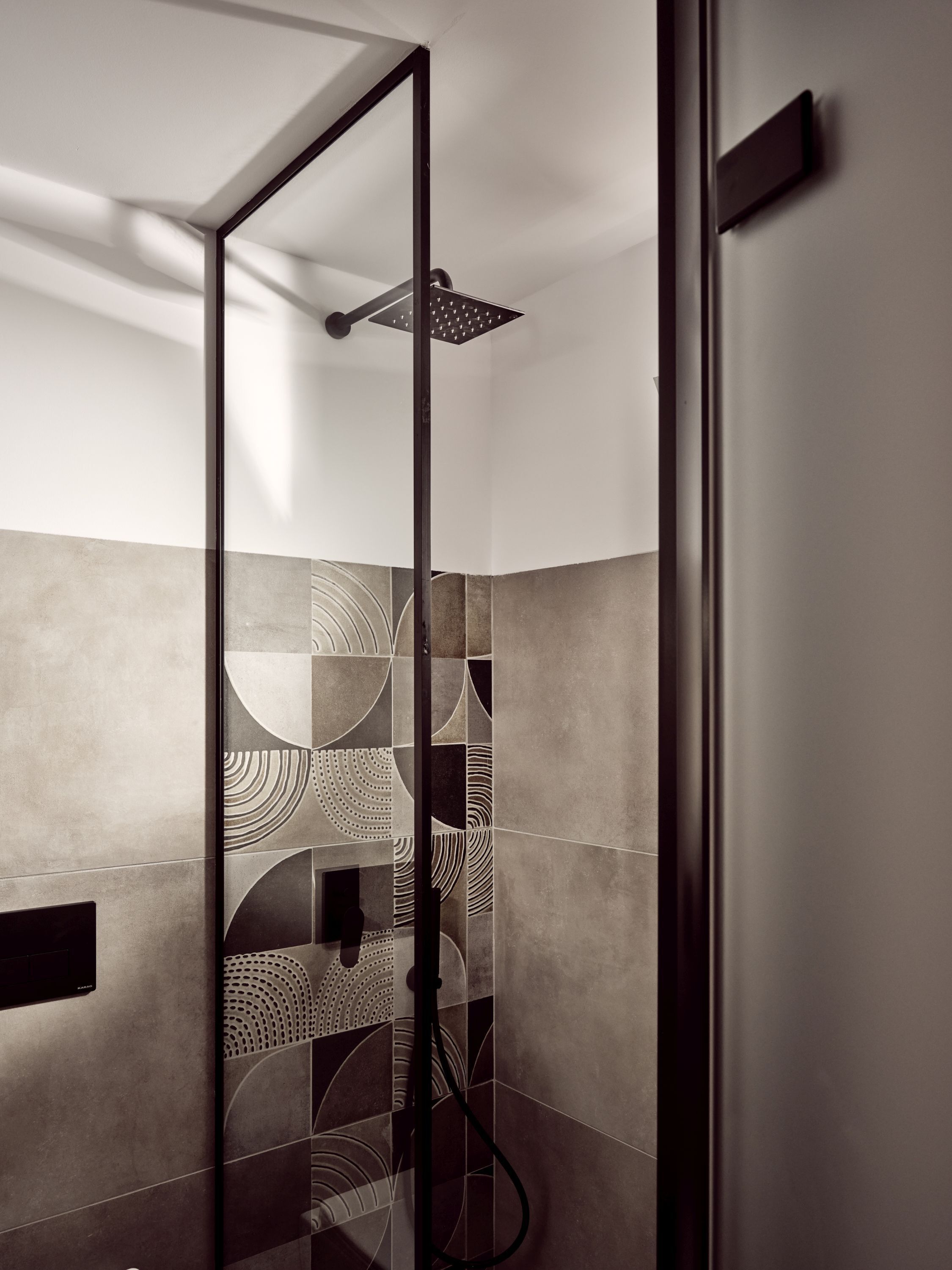 A modern shower with a glass door, geometric tile patterns on the walls, and a visible showerhead.