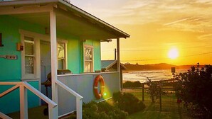 Una casa turquesa amb un porxo, una barra de socorristes i vistes a l'oceà al capvespre.