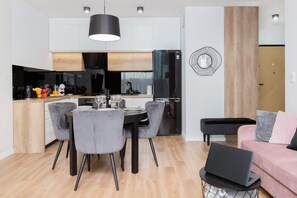A modern kitchen with a dining area, a laptop on a side table, and a sofa in the living area.