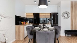 Une cuisine moderne avec un coin repas, comprenant un luminaire suspendu noir, des chaises à revêtement gris et une table à manger noire pour quatre personnes.