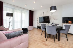 Una sala de estar moderna con un sofá, una mesa de comedor, sillas, un televisor de pantalla plana y una lámpara.