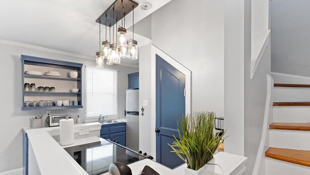 A modern kitchen with a central island, built-in shelves, and a blue door.