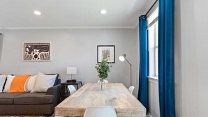 A modern living room with a wooden dining table, a grey sofa, and a blue curtain.