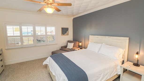 A bedroom with a bed, a nightstand, a chair, a ceiling fan, and a window with blinds. - Creston House 3C~Sunrise to Sunset, the Upper Deck is the Place to be (St. Augustine)