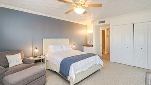 Ein Schlafzimmer mit einem Bett, einem Nachttisch, einem Sessel, einem Deckenventilator und einem begehbaren Kleiderschrank.
