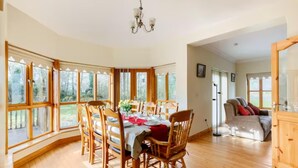 A dining area with wooden chairs and a table set for four, large windows, and a chandelier. - Large Country House, Sleeps 10, Family Friendly (Westport)