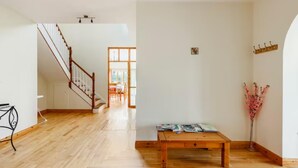 A spacious room with a wooden floor, a staircase, a dining area with a table and chairs, and a wall-mounted shelf. - Large Country House, Sleeps 10, Family Friendly (Westport)