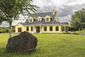 A yellow house with a large rock in the foreground, surrounded by green grass and trees. - Large Country House, Sleeps 10, Family Friendly (Westport)