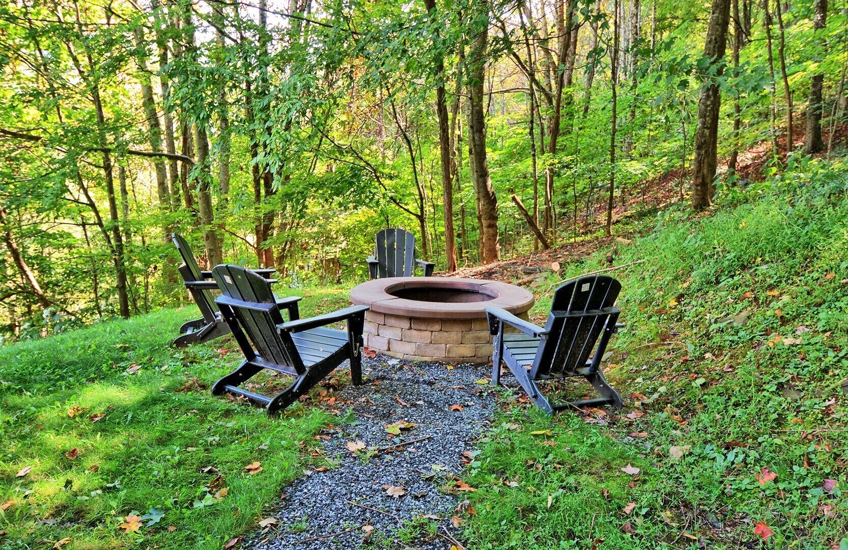 An outdoor seating area with Adirondack chairs and a stone fire pit surrounded by a gravel path.