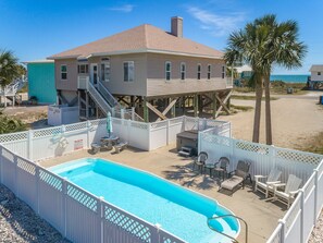 A two-story house with a pool, outdoor seating, and a view of the beach.