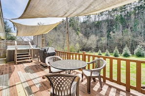 Une terrasse en bois, dotée de mobilier d’extérieur, d’un barbecue et offrant une vue sur une zone boisée.