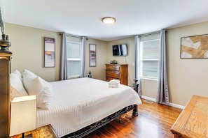 Une chambre bien rangée, avec un lit, une commode et un téléviseur fixé au mur.
