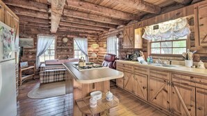 A rustic cabin interior with a wooden dining table, a sofa, and a kitchen area with wooden cabinets and a large window. - Quaint & Quiet Belleview Cabin on 35 Acres! (Belleview)