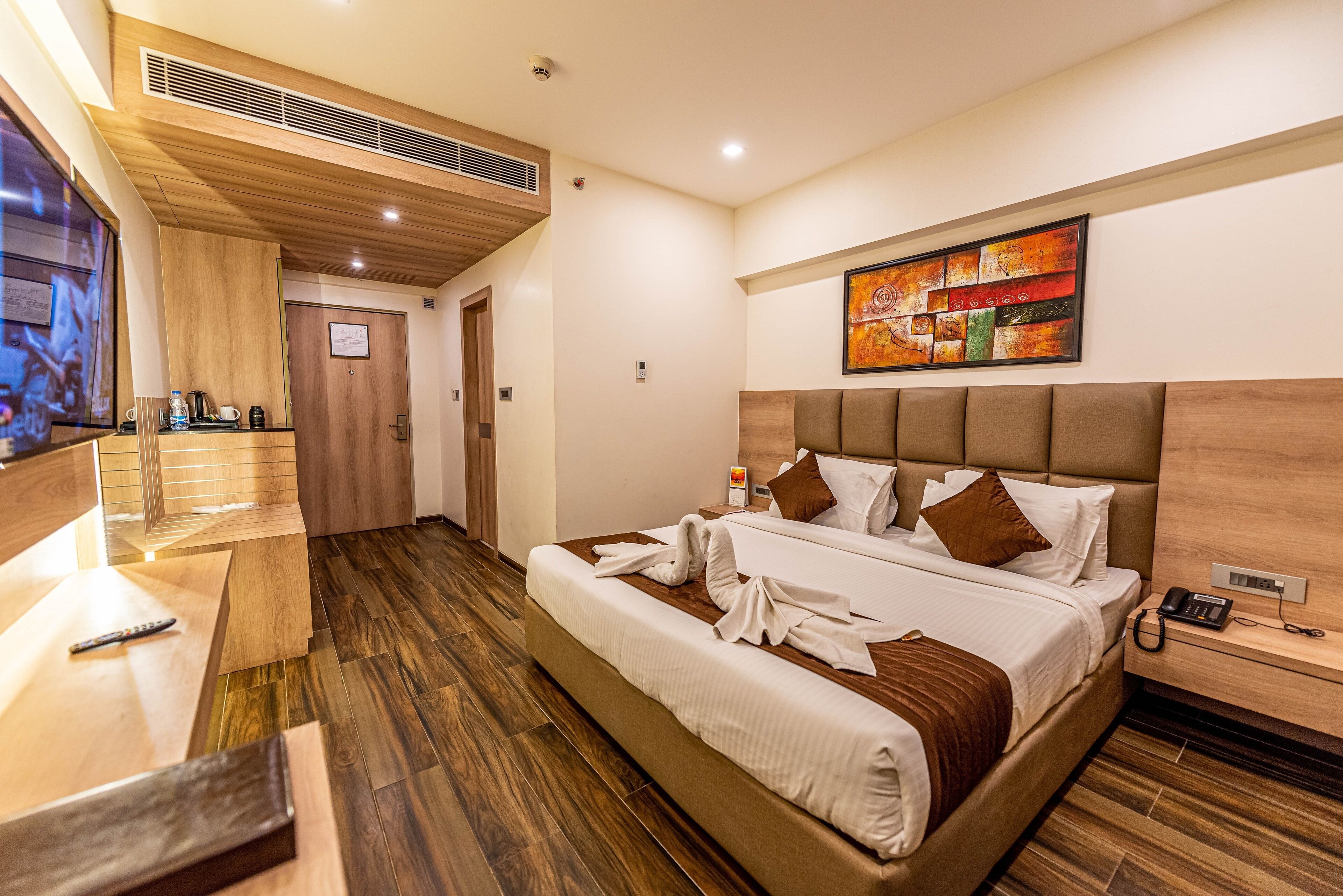 Una habitación de hotel moderna con una cama grande, un cabecero de madera, una mesita de noche con un teléfono y un cuadro en la pared.