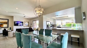 A modern kitchen with a central island, a dining area with teal chairs, and a large window offering a view of the outdoors.