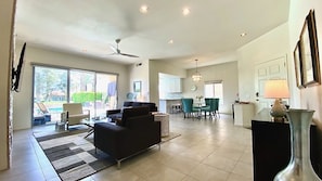 A spacious living area with a sofa, a dining table with chairs, a kitchen in the background, and a ceiling fan.