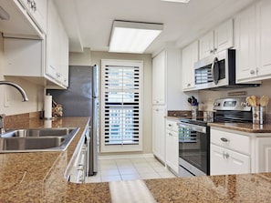 Una cocina moderna con armarios blancos, electrodomésticos de acero inoxidable y encimeras de granito.