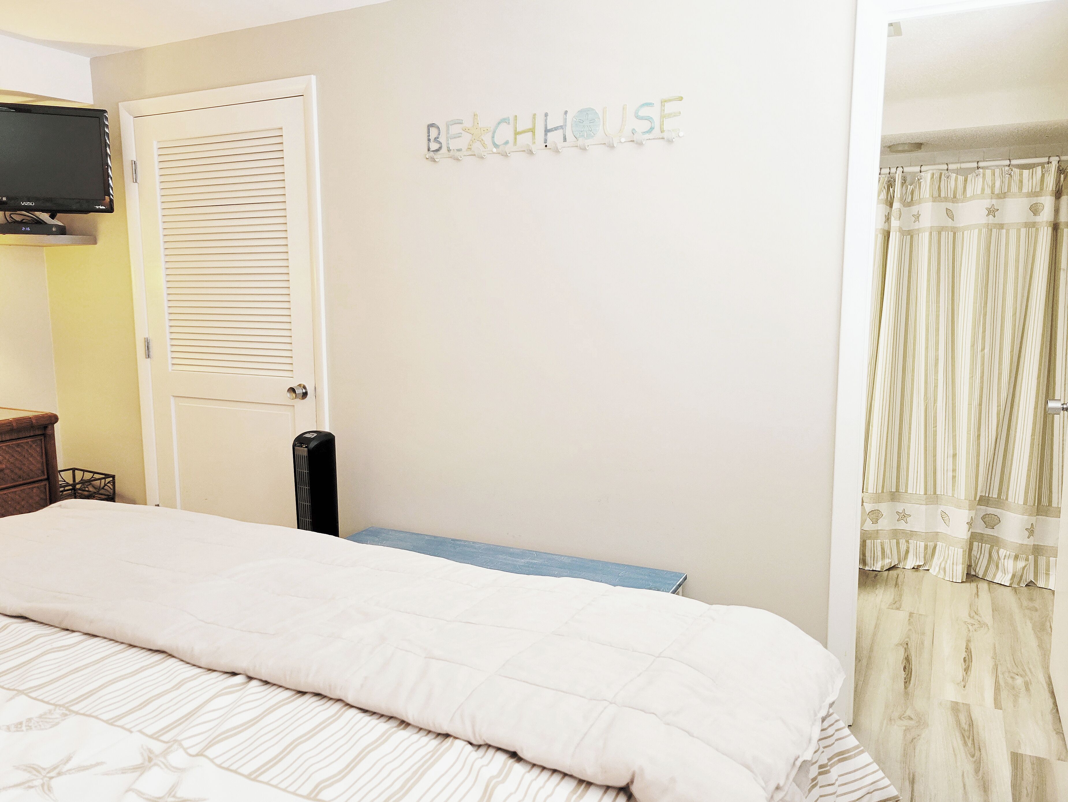 Une chambre avec un lit, un téléviseur fixé au mur, une porte et une pancarte sur laquelle on peut lire : « MAISON DE PLAGE ».
