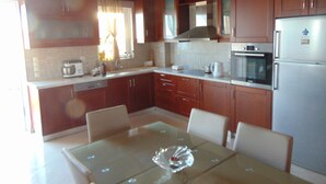A kitchen with wooden cabinets, a refrigerator, a microwave, and a dining table with chairs. - Litinas Casa-In front of the Sea (Chania)