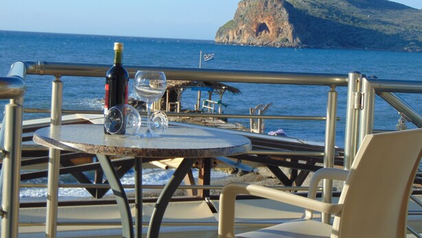 A table with a bottle and glasses, overlooking a body of water and a rocky island. - Litinas Casa-In front of the Sea (Chania)