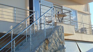 A building with a stone facade, metal railings, and a staircase leading to a balcony. - Litinas Casa-In front of the Sea (Chania)